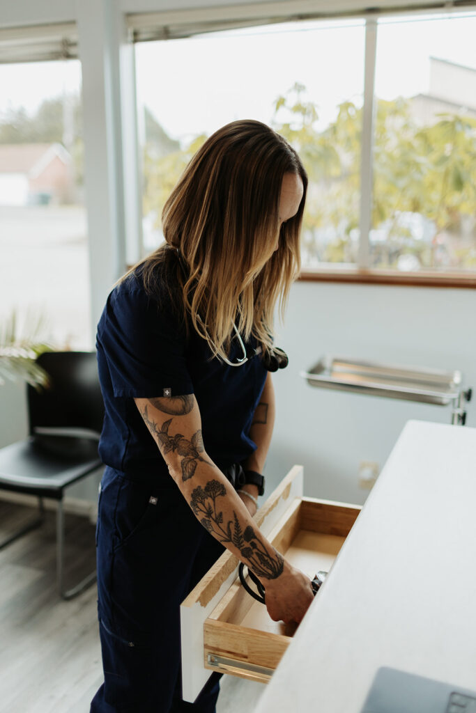 woman in black scrubs and arm tattoos looks in open drawer