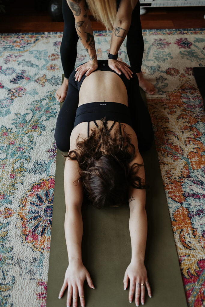 woman leans forward on yoga mat with some pressing down on lower back