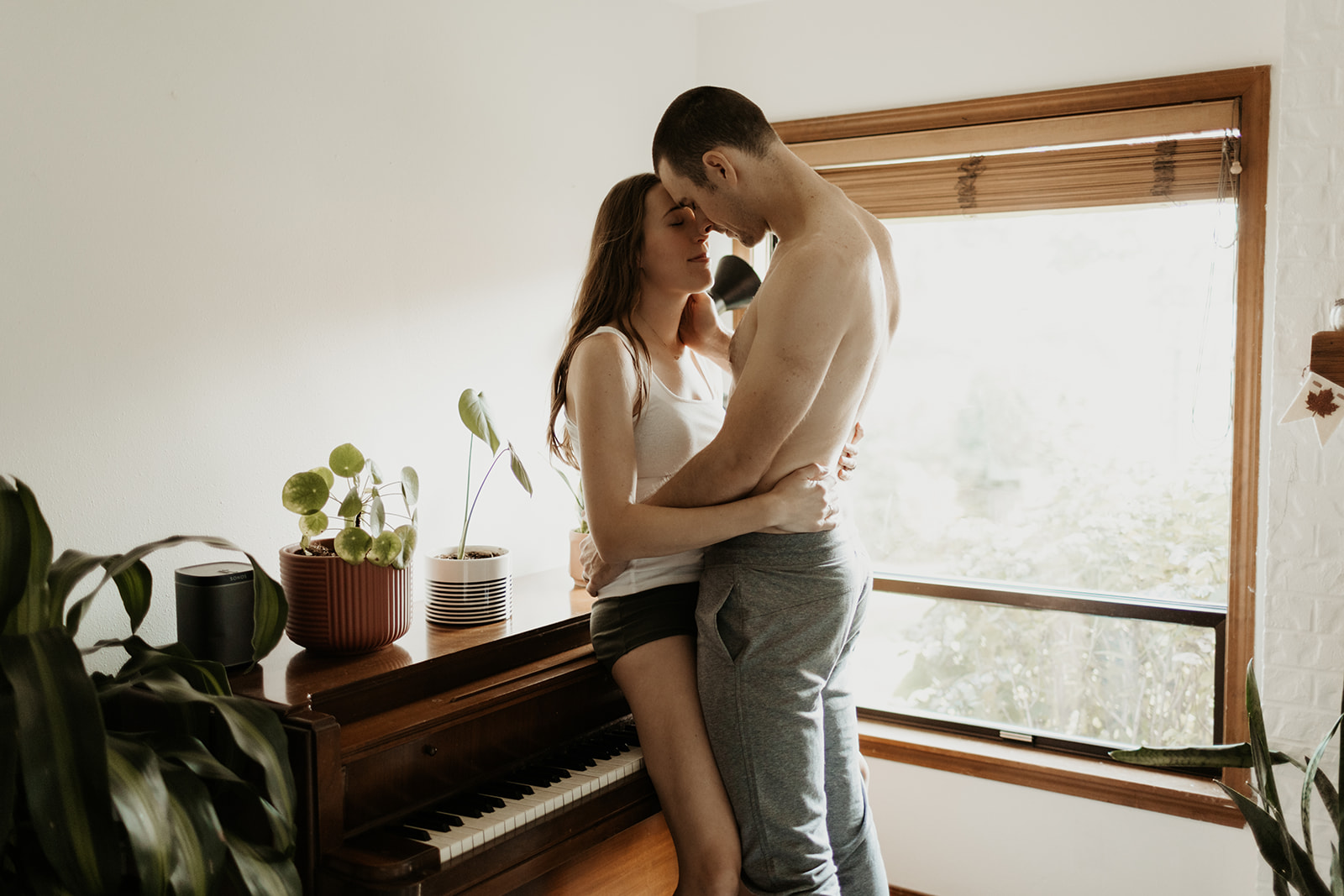 shirtless man and woman hold each other while leaning against piano