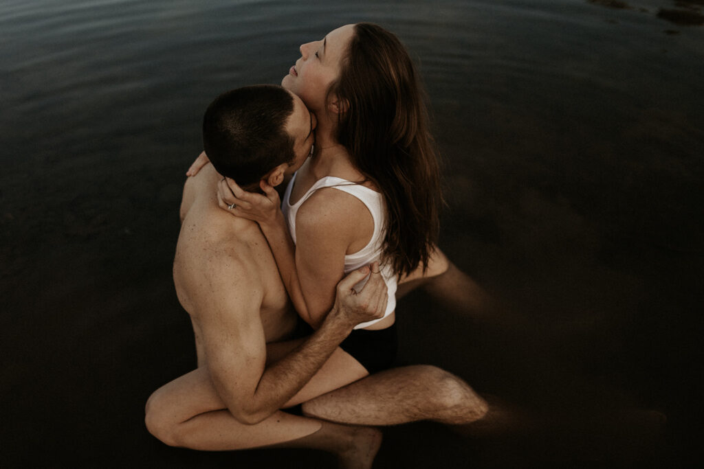 woman straddles man in water as he kisses her neck