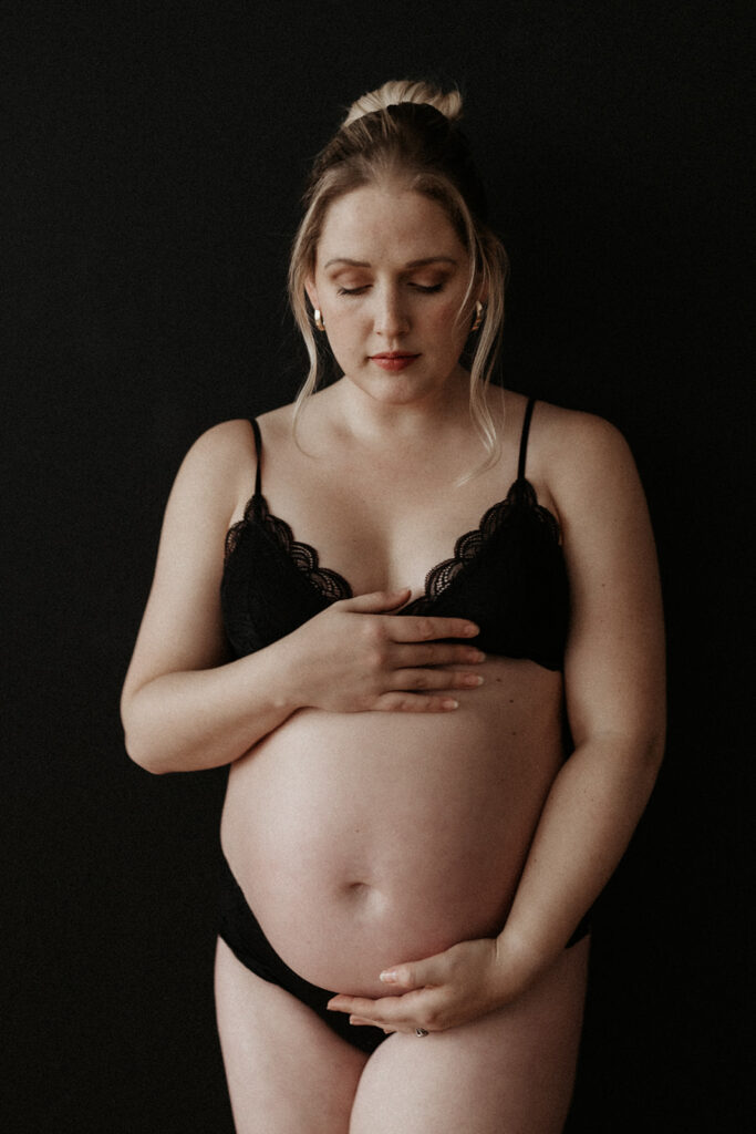 maternity boudoir, pregnant woman holding stomach wearing a black bra and underwear