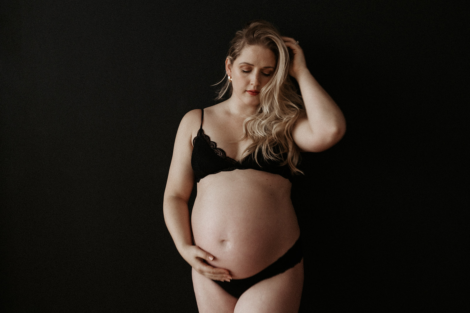 maternity boudoir, pregnant woman holding stomach wearing a black bra and underwear