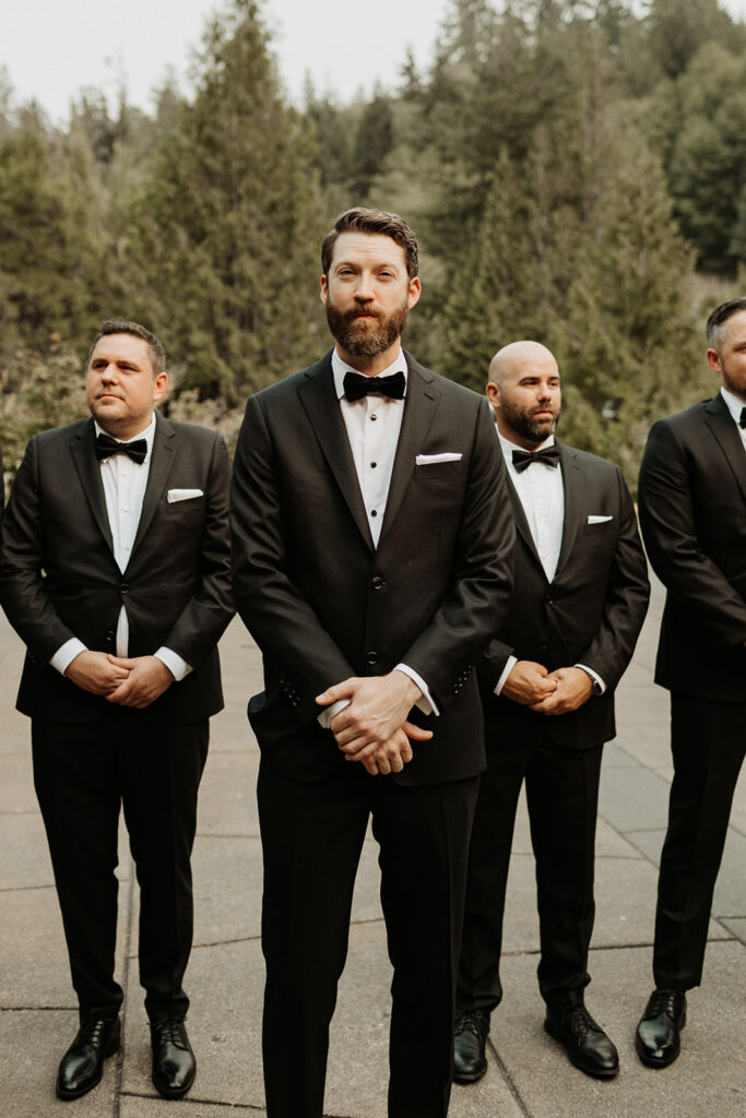 groom in black tux stands with groomsmen