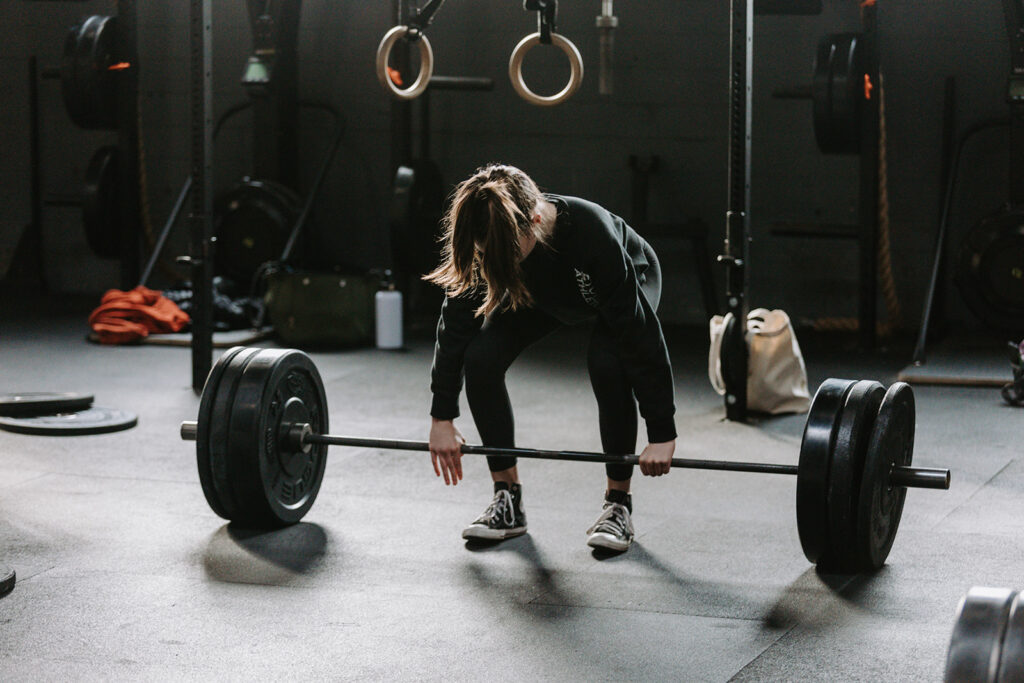 woman leans down to pick up barbell