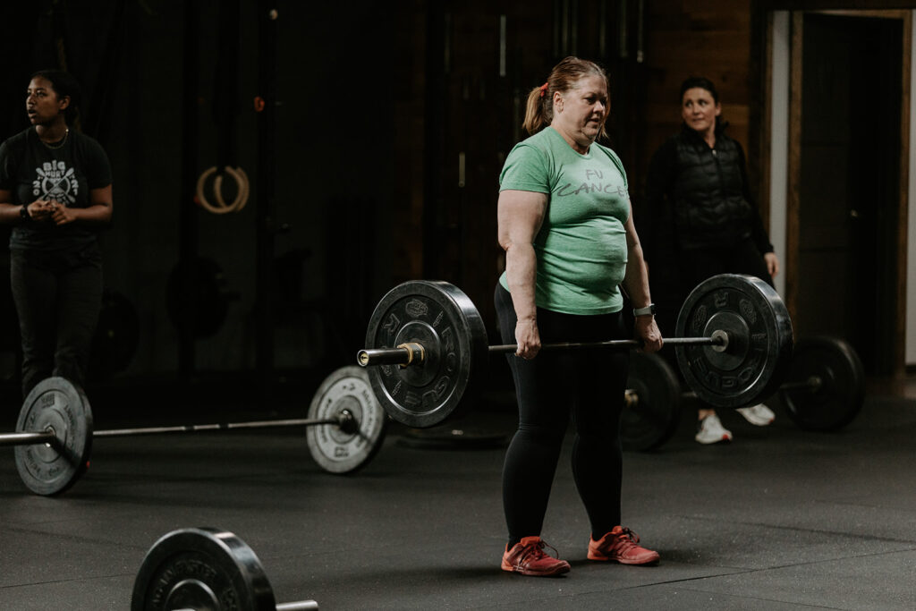 woman in a gym standing holding a barbell with weights on it